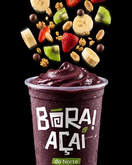 Copo de açaí com frutas caindo sobre fundo preto